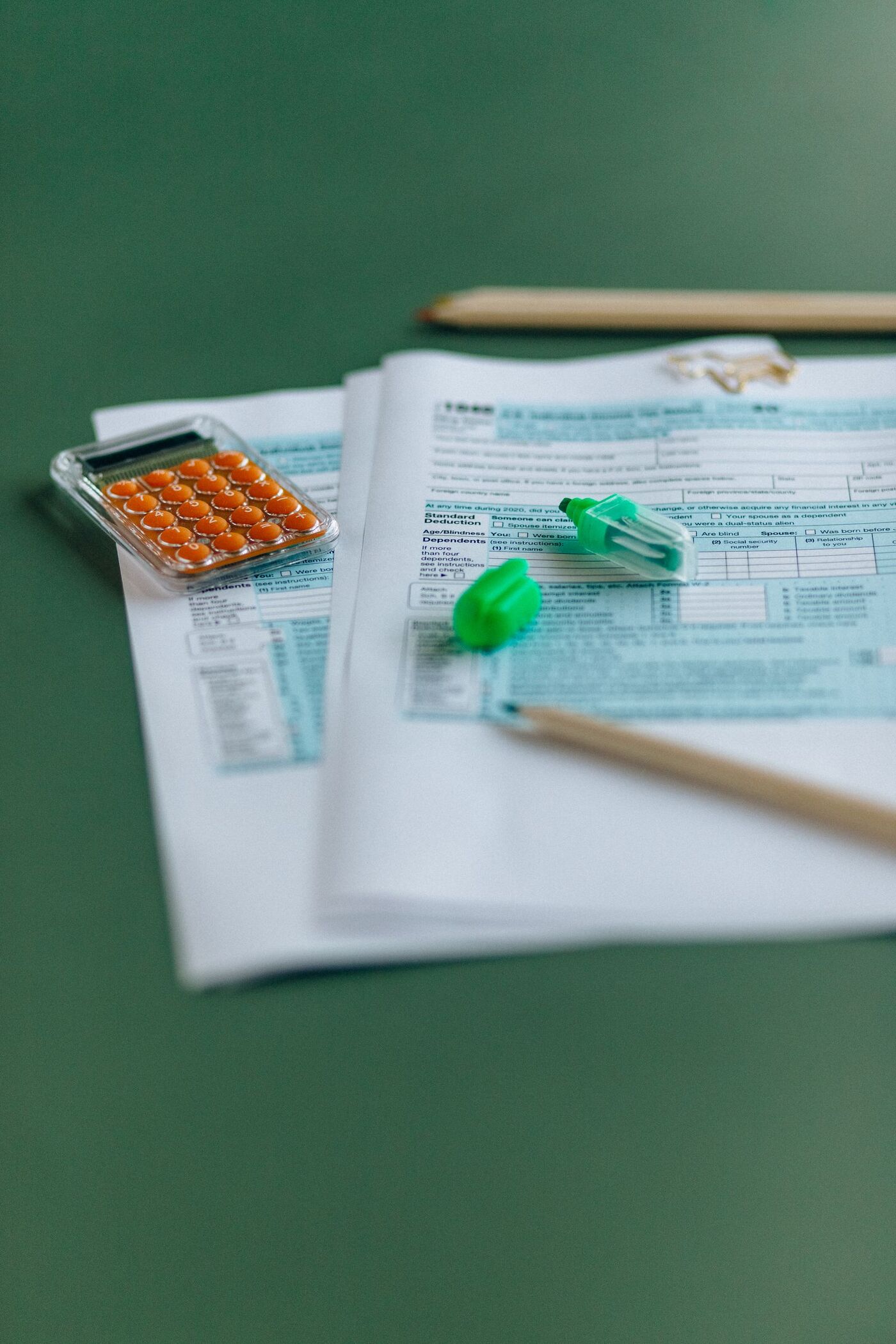 Printed tax forms on a green table with a pencil and highlighters